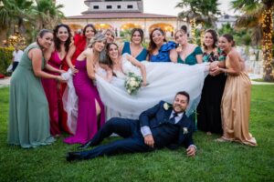 Lo sposo disteso sull'erba con una rosa tra i denti, damigelle che ridono sorreggendo lo strascico